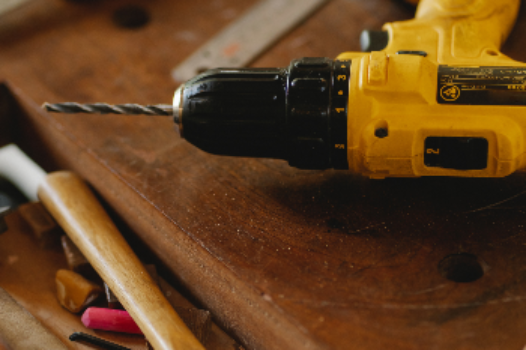 yellow drill sitting on top of wooden planks and hammers